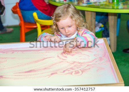 Cute child girl drawing draws developing sand in preschool at table in kindergarten by method of Montessori