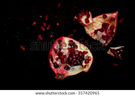 Pomegranate and pieces of ripe pomegranate with grains on a dark background