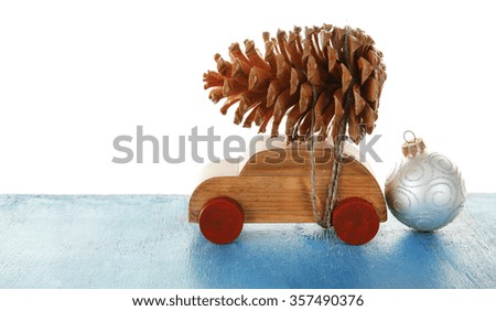 Wooden toy car with pine cone and bauble on a table over white background