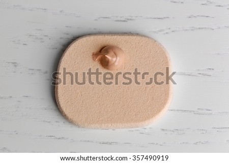 Makeup sponge with liquid foundation on wooden background