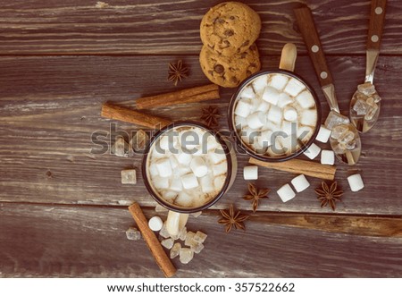 Two mugs filled with hot chocolate and marshmallows at the old wooden table with cinnamon and brown sugar. Top view. Vintage toned picture.