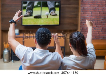 Asian Couple having fun watching golf game in living room