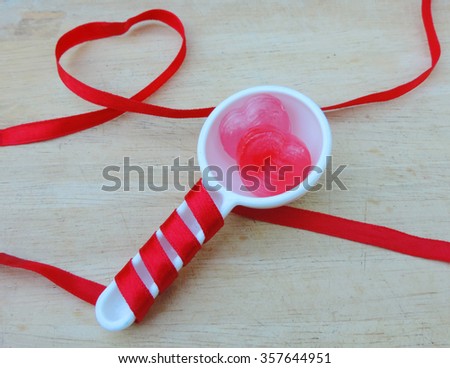 Valentines Day background with two hearts in white spoon and hearts of ribbon on wooden table.          