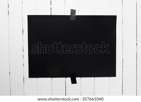 Blank black poster hanging on a tape on white wooden plank wall. Template background for your design.