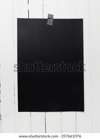 Blank black poster hanging on a tape on white wooden plank wall. Template background for your design.