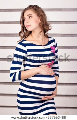 Pregnant woman in a striped dress on a white background. Pregnancy. Studio.