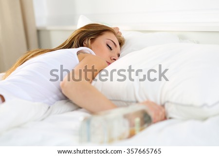 Blonde young woman lying in bed deadly drunken holding near-empty bottle of booze. Female intoxicated with alcohol after tough night party. Alcoholism, habitual drunkenness, pernicious habit concept