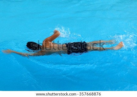 Asian kid swims in swimming pool - front crawl style back view