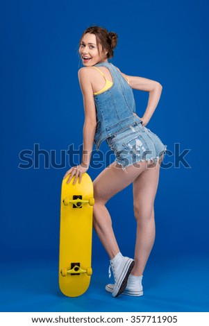 Full length portrait of a happy young woman with skateboard posing over blue background