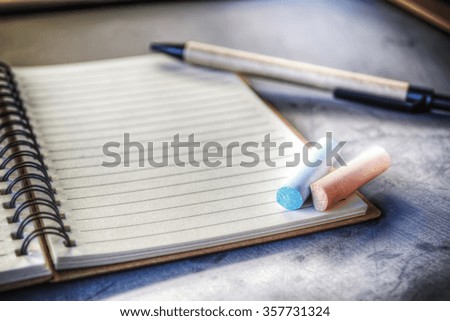 notebook, pen and chalks on a blackboard