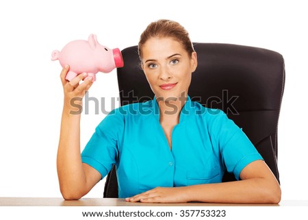 Young female doctor or nurse holding piggybank.