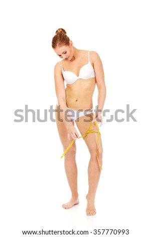 Young slim woman measuring her thigh with a yellow tape.