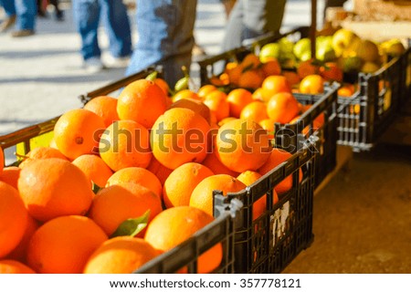 Closeup picture of fresh oranges on the market sunny day background with customers walking by