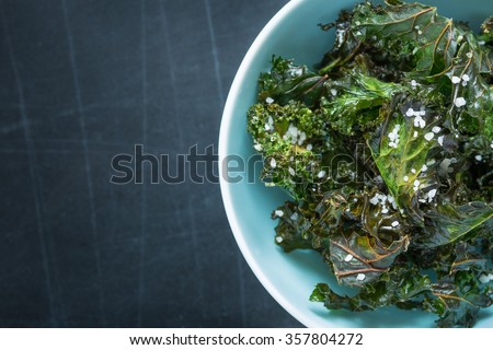 Kale chips with salt in pastel blue bowl captured from above (top view). Healthy dietetic snack. Black chalkboard as background. Background layout with free text space. Royalty-Free Stock Photo #357804272