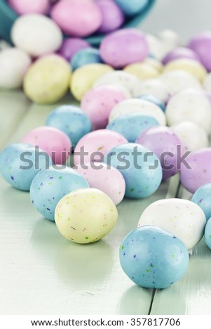A blue tin bucket tipped over, spilling Easter candy eggs onto a table. Shallow depth of field with selective focus on closest candy eggs.
