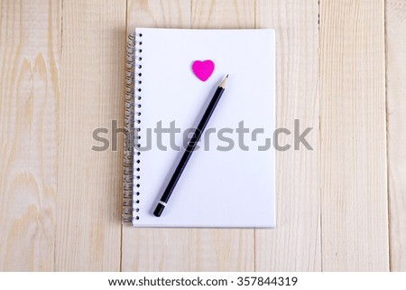 Open a blank Notepad and a pink heart on white wooden table. Valentine's day background. Free space for text. Top view