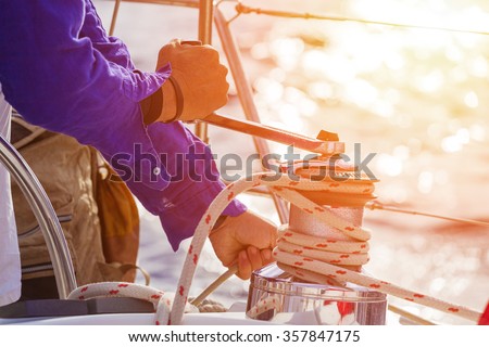 Closeup up of Yachtsman hands dealing with yacht ropes .Lens flare, unrecognizable person Royalty-Free Stock Photo #357847175