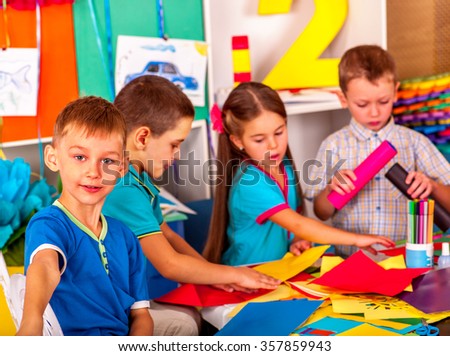 Kids holding colored paper on table in kindergarten .