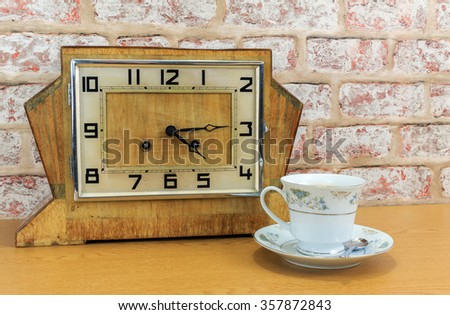 Vintage art deco wooden mantel clock with old  brick wall effect background and china teacup and filled with tea   