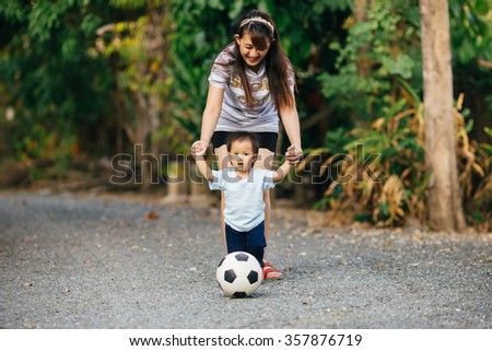Mother practices her child to play a soccer football: film tone picture style.
