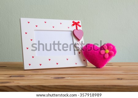 White vintage photo frame with pink heart on wooden table over wall grunge background, Valentine day concept.