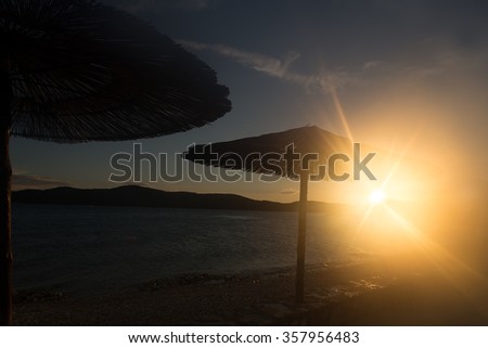 Photo closeup with sun spot of seascape with beach umbrellas for sun protection in line at seashore silhouetted against sunset background, horizontal picture