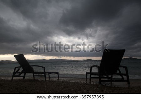 Photo closeup of two chaise lounges day beds standing on pebbles on beach at dusk low dark clouds bad weather grey sea shore against seascape background, horizontal picture