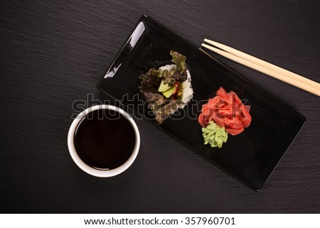 Healthy japanese food concept. Vegetarian sushi roll with vegetables, soy sauce, and chopsticks over black stone table. Top view. Selective focus