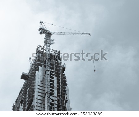 Working crane on a modern office building under construction against blue sky in Singapore. Asian urban development and construction concept. Industrial background