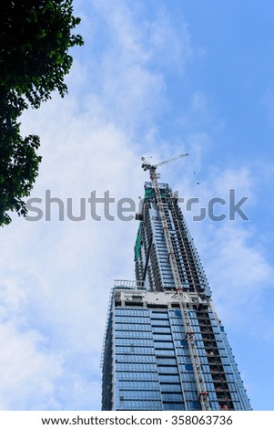 Working crane on a modern office building under construction against blue sky in Singapore. Asian urban development and construction concept. Industrial background