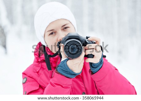 the girl with the camera on the background of winter snow. The bright colored jacket. Photographer with the camera.