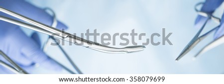 Close-up of doctor's hands holding surgical clamps. Medical background. Letter box format