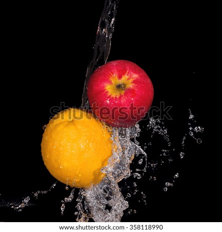 apple and orange with splashes of water on a black background