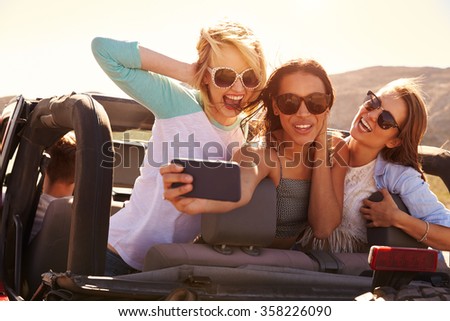 Female Friends On Road Trip In Convertible Car Taking Selfie