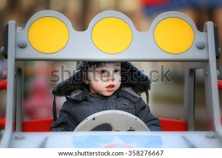 Cute little boy in cap with ear-flaps driving a toy car in Russia. Image with toning and selective focus