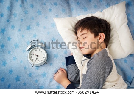 six years old child sleeping in bed with alarm clock Royalty-Free Stock Photo #358291424