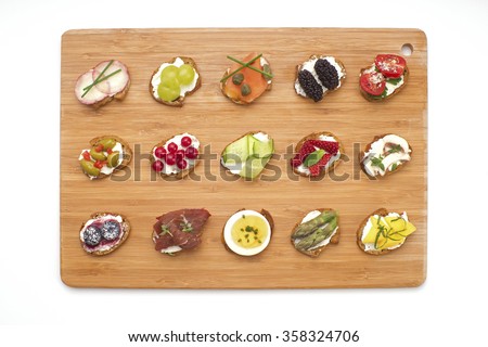 Open canape sandwiches and bite size crostinis on a wooden serving board. Party food crackers with toppings isolated on white. Royalty-Free Stock Photo #358324706