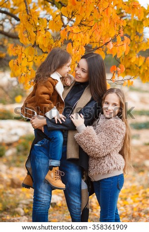 Beautiful Young Woman with Two Children Outside. Three sisters girls in park. happy family outdoors. woman and two children having fun. Autumn. Mother and daughter in the park. Happy parent and kids