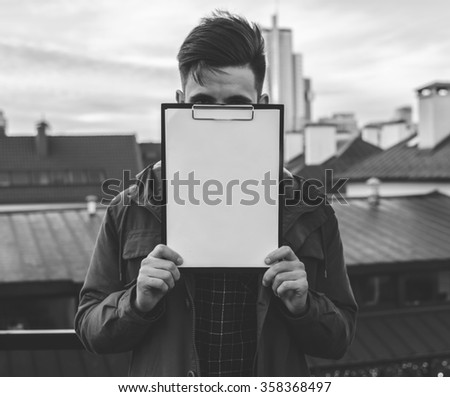 Black and white photo of the young man holding white empty paper on the city street