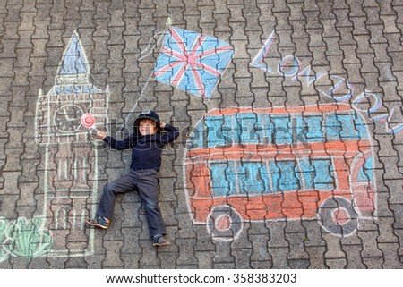 Happy little kid boy in british policeman uniform having fun with London picture drawing with colorful chalks. With Big Ben, Union Jack and red bus.