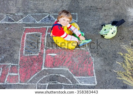 Creative leisure for kids: adorable child of four years having fun with fire truck picture drawing with chalk, outdoors. Dreaming of future profession.