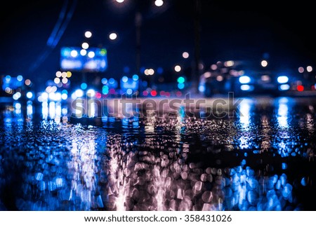 Rainy night in the big city, the light from the headlamps of approaching car on the highway. View from the level of asphalt, in blue tones