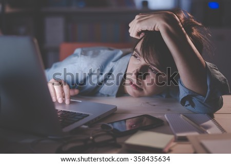 Sleepy exhausted woman working at office desk with her laptop, her eyes are closing and she is about to fall asleep, sleep deprivation and overtime working concept Royalty-Free Stock Photo #358435634