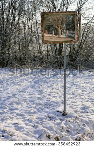 Old traffic mirror in winter with snowy landscape.