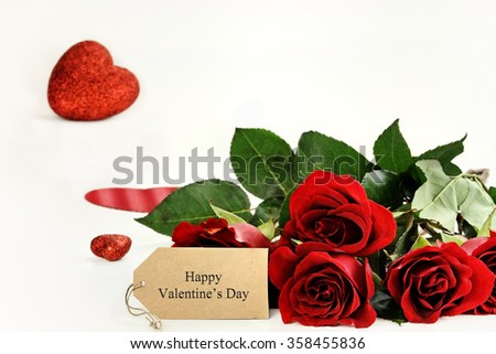 Red roses with an Happy Valentines Day label and glitter hearts in the background. Room for copy space with extreme shallow depth of field.