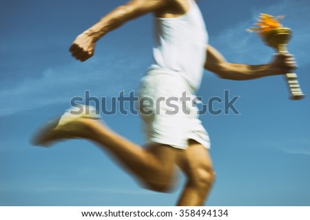 Torchbearer in old fashioned white uniform running with sport torch in motion blur across sunny blue sky