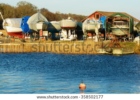 Boats in winter storage covered with tarps and supported by scaffolding. Winter storage on land protects the boats from the sea ice that could otherwise cause damage to the keels. Royalty-Free Stock Photo #358502177