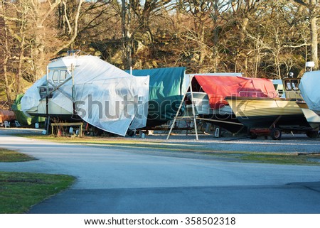 Boats in winter storage covered with tarps and supported by scaffolding. Winter storage on land protects the boats from the sea ice that could otherwise cause damage to the keels. Royalty-Free Stock Photo #358502318