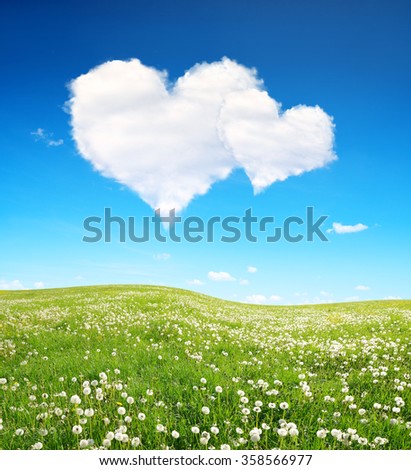 Spring meadow and blue sky with a white clouds in the form of heart. Valentines day.