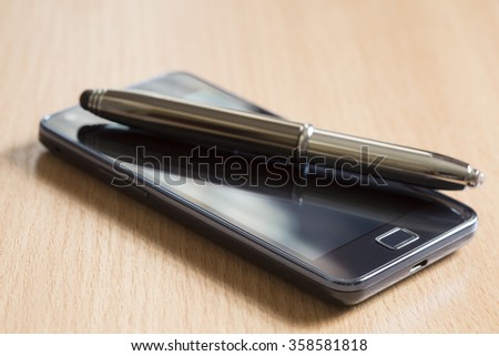 Mobile phone and a pen on wooden background